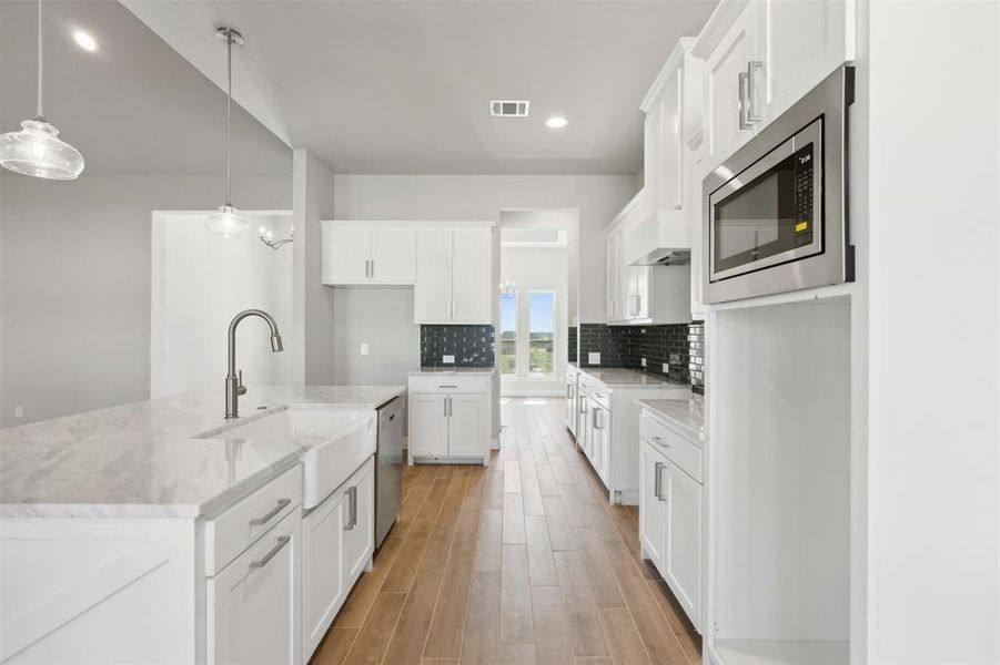 Kitchen with tasteful backsplash, stainless steel appliances, decorative light fixtures, and white cabinets