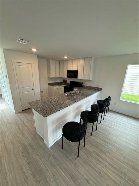 Kitchen featuring light hardwood / wood-style floors, electric range, white cabinetry, and kitchen peninsula