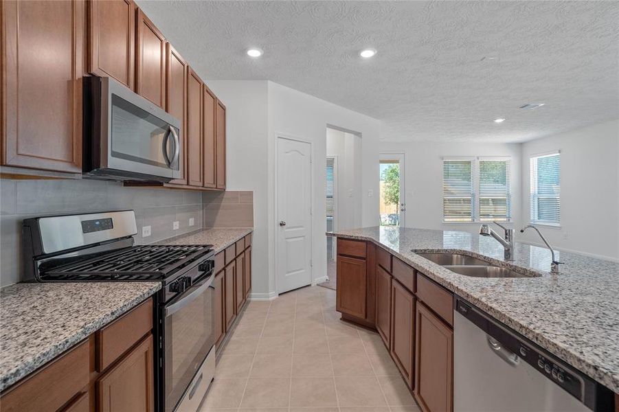 This spacious kitchen features high ceilings, stained wood cabinets, granite countertops, SS appliances, modern tile backsplash, recessed lighting, and pantry all overlooking your huge family room.