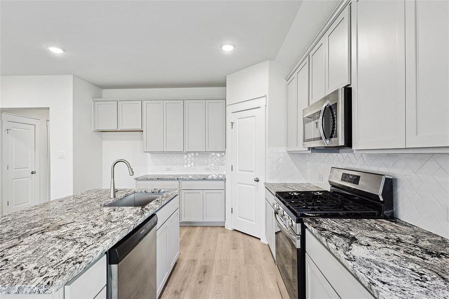 Kitchen with light hardwood / wood-style flooring, backsplash, sink, an island with sink, and appliances with stainless steel finishes