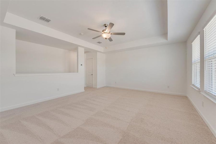 Carpeted empty room with ceiling fan and a raised ceiling