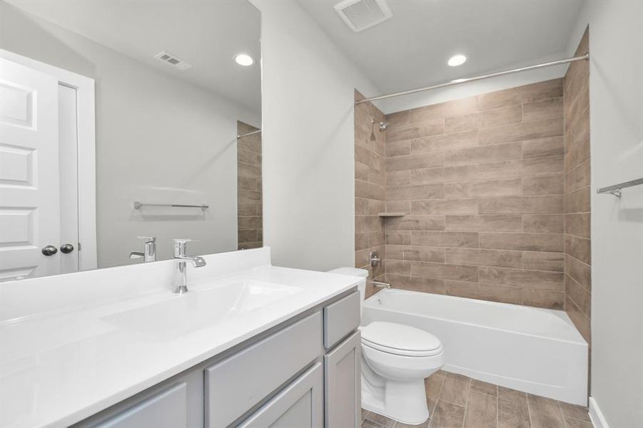 Experience sophistication in the secondary bathroom, where tile flooring complements a bath/shower combo with tile surround.