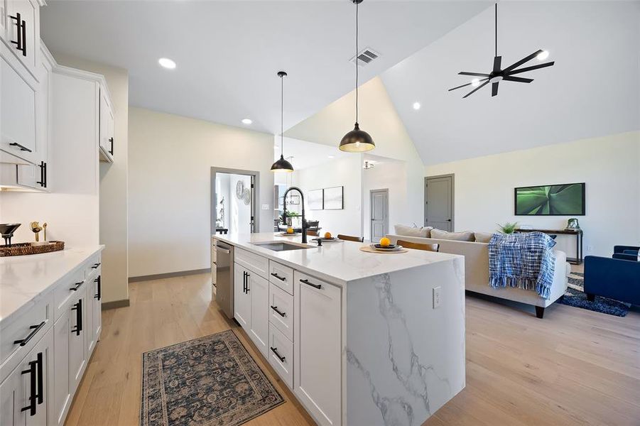 Kitchen with a kitchen island with sink, sink, stainless steel dishwasher, white cabinetry, and high vaulted ceiling