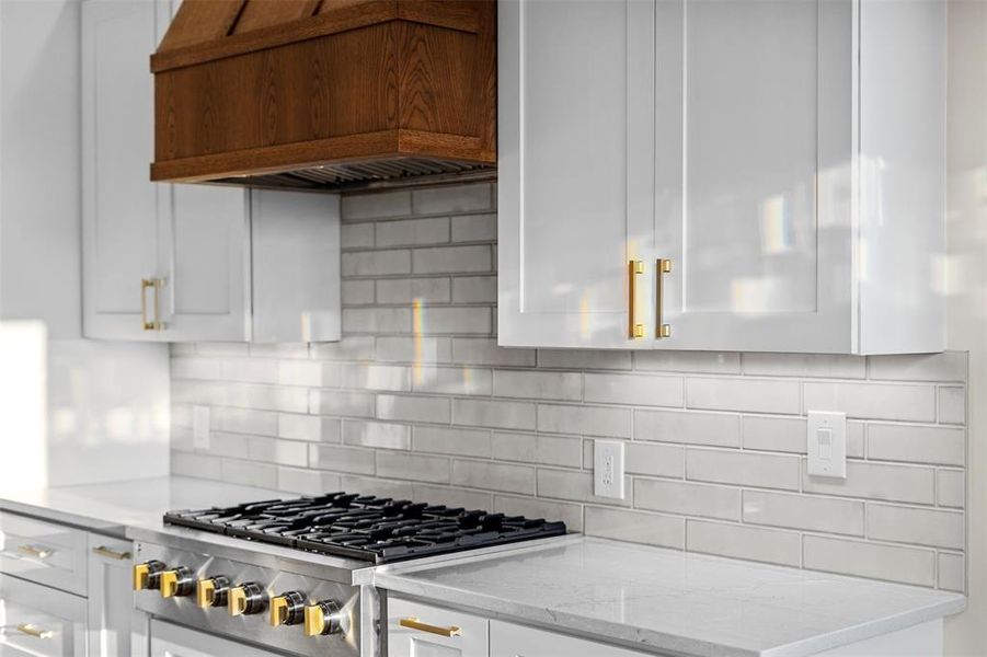 Kitchen with decorative backsplash, stainless steel gas cooktop, light stone counters, and white cabinetry