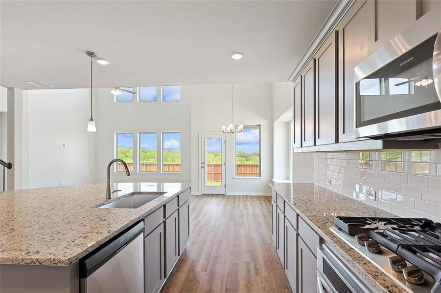 Kitchen featuring light hardwood / wood-style flooring, stainless steel appliances, sink, pendant lighting, and light stone counters