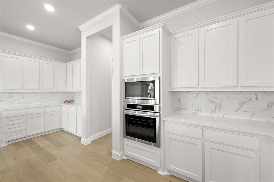 Kitchen featuring white cabinets, light hardwood / wood-style flooring, ornamental molding, and tasteful backsplash