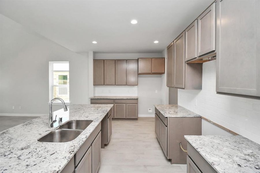 Culinary haven, featuring granite countertops, a tile backsplash, stainless steel appliances (to be installed), 42” upper cabinets, and bright recessed lighting. Sample photo of completed home. Actual colors and selections may vary.