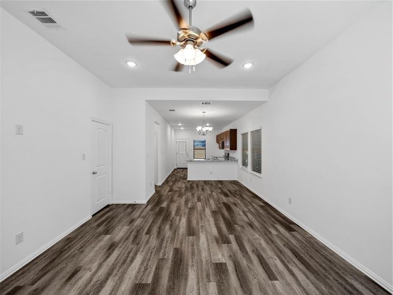 Unfurnished living room with dark wood-type flooring and ceiling fan with notable chandelier