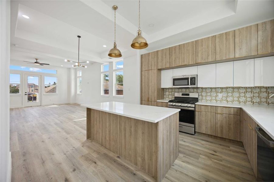 Spacious, modern kitchen featuring light cabinetry, white countertops, and stainless steel appliances. Enjoy an oversized island, pendant lighting, and ample natural light streaming in from the large windows. The open floor plan allows for an easy flow into the adjacent living area!