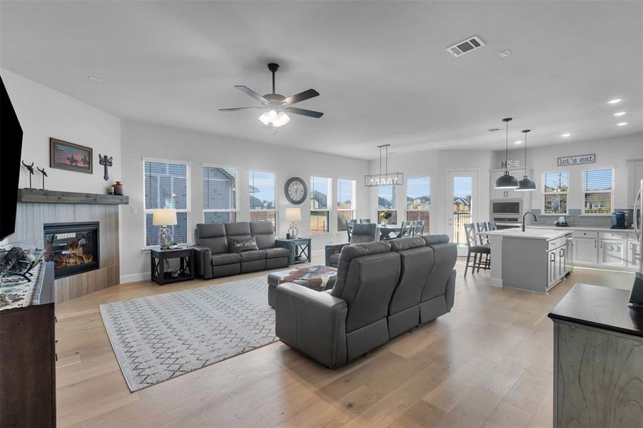 Living room featuring light wood-type flooring, a tiled fireplace, and ceiling fan