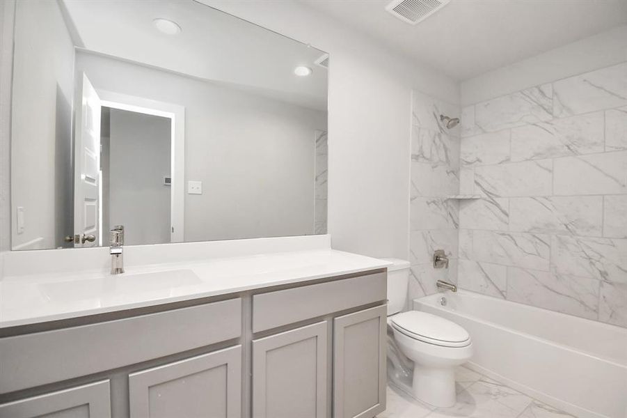 Sophistication in the secondary bathroom, where tile flooring complements a bath/shower combo with tile surround. Light wood cabinets complete with a beautiful light countertop, enhances the space for a truly inviting ambiance.