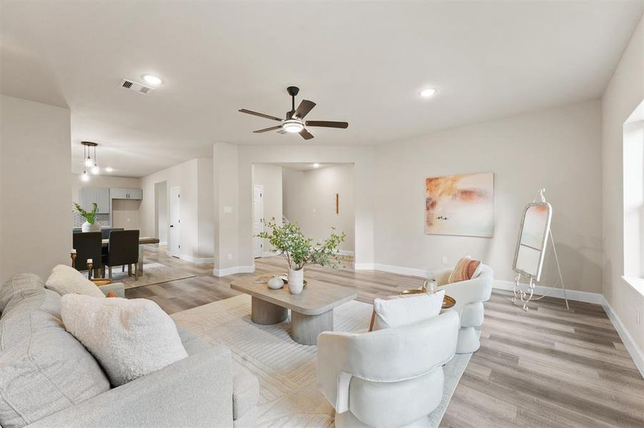 This is a bright and spacious open-plan living area featuring neutral colors, modern furnishings, and wood flooring, with ample natural light and a view into the dining and kitchen spaces.