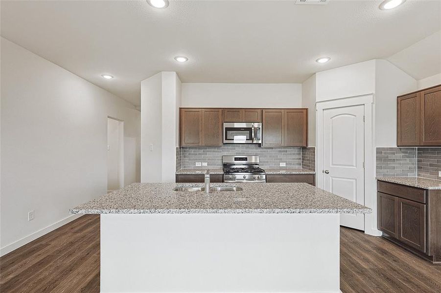 Kitchen with backsplash, appliances with stainless steel finishes, a kitchen island with sink, dark wood-type flooring, and sink