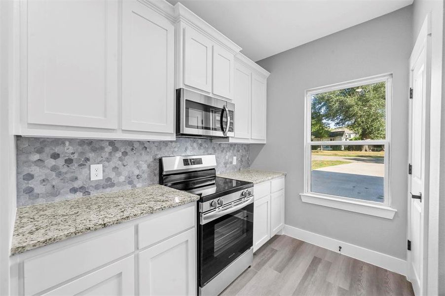 Kitchen featuring decorative backsplash, white cabinets, light stone countertops, stainless steel appliances, and light hardwood / wood-style flooring