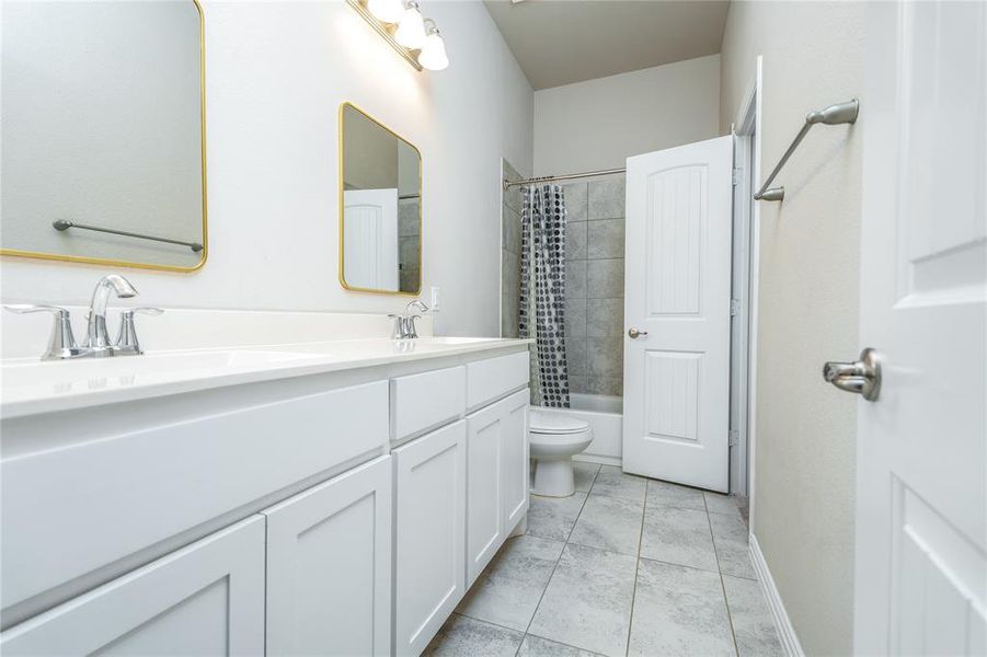 Full bathroom featuring shower / tub combo with curtain, toilet, tile patterned floors, and double sink vanity