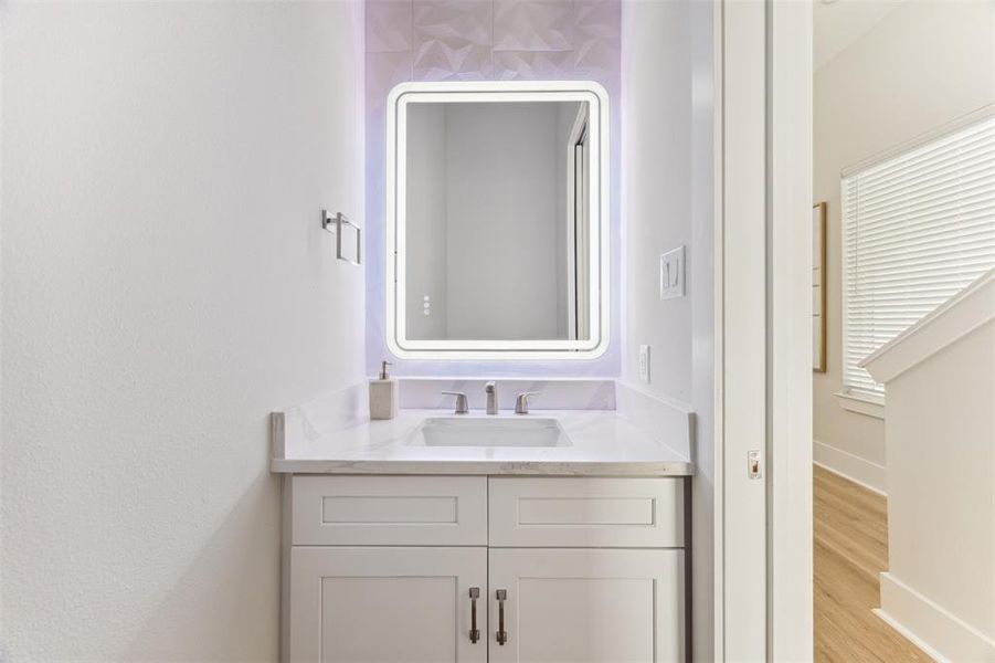 Powder room tucked away from the living area features a lighted mirror and quartz vanity.