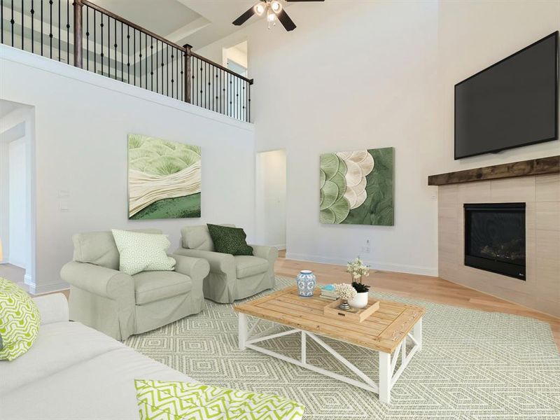 Virtually staged photo - Living room with a tile fireplace, ceiling fan, light hardwood / wood-style floors, and a towering ceiling