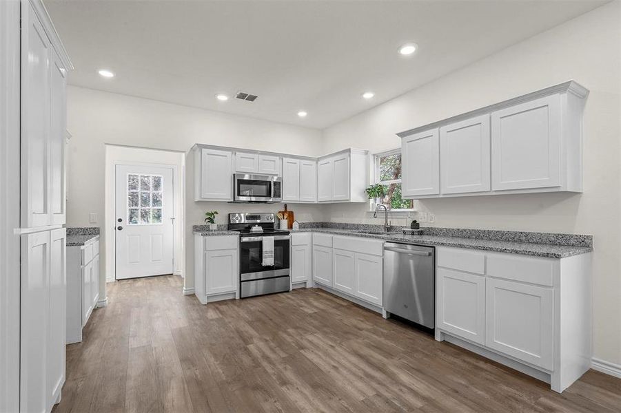 Kitchen with stainless steel appliances, a healthy amount of sunlight, hardwood / wood-style floors, and white cabinets