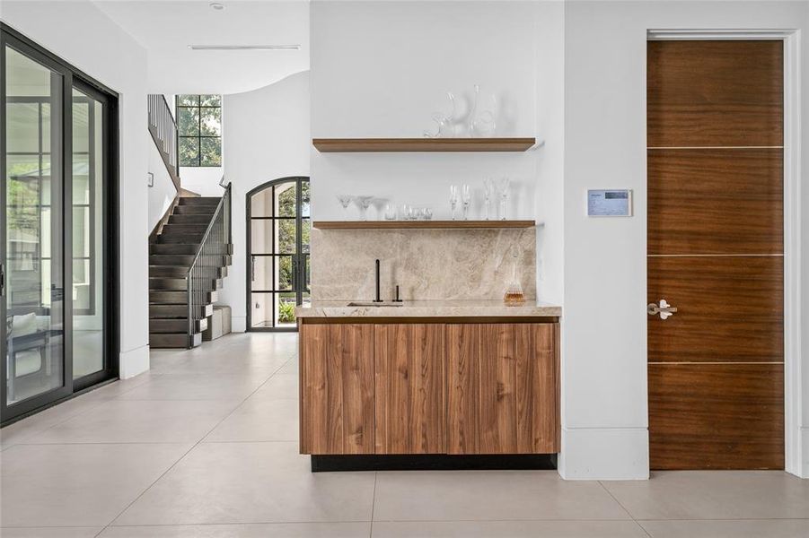 The wet bar showcases Taj Mahal quartzite countertops and backsplash and custom Madeval cabinetry. The overall design is functional yet stylish, perfect for both everyday use and entertaining.