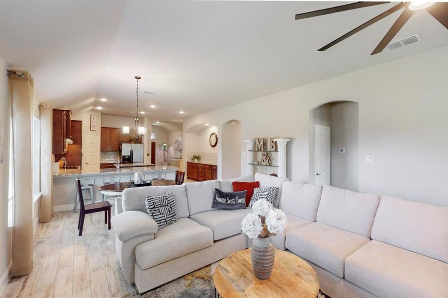 Living room with ceiling fan with notable chandelier, vaulted ceiling, and light hardwood / wood-style flooring