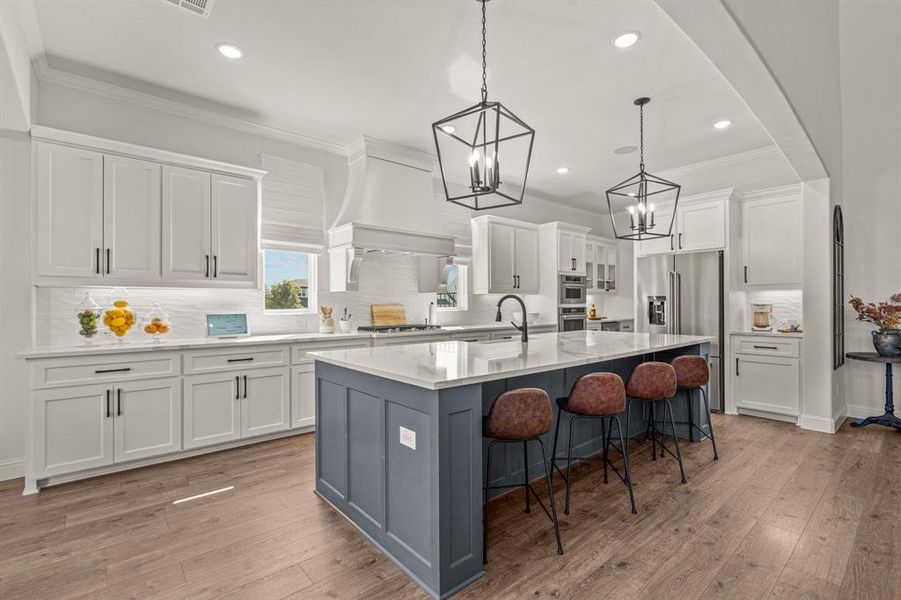 Kitchen with appliances with stainless steel finishes, pendant lighting, white cabinets, light hardwood / wood-style flooring, and a center island with sink