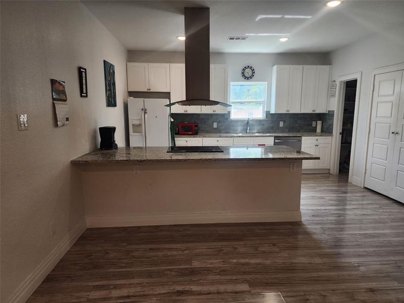 Kitchen with black appliances, island range hood, dark hardwood / wood-style flooring, white cabinetry, and dark stone counters