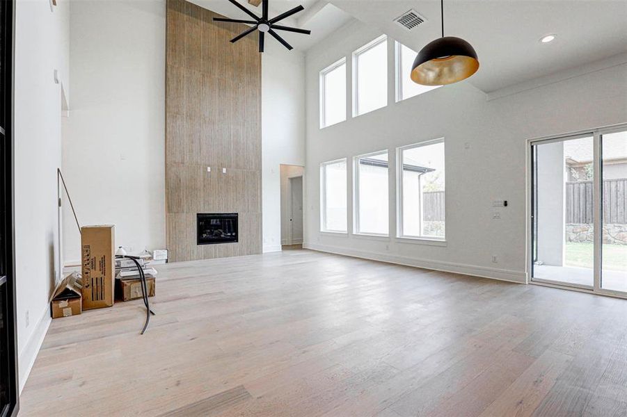 Unfurnished living room with a fireplace, light hardwood / wood-style flooring, a wealth of natural light, and a high ceiling