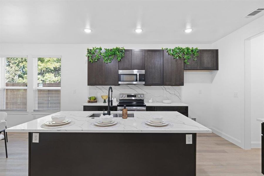 Kitchen with light hardwood / wood-style floors, light stone countertops, stainless steel appliances, and a center island with sink