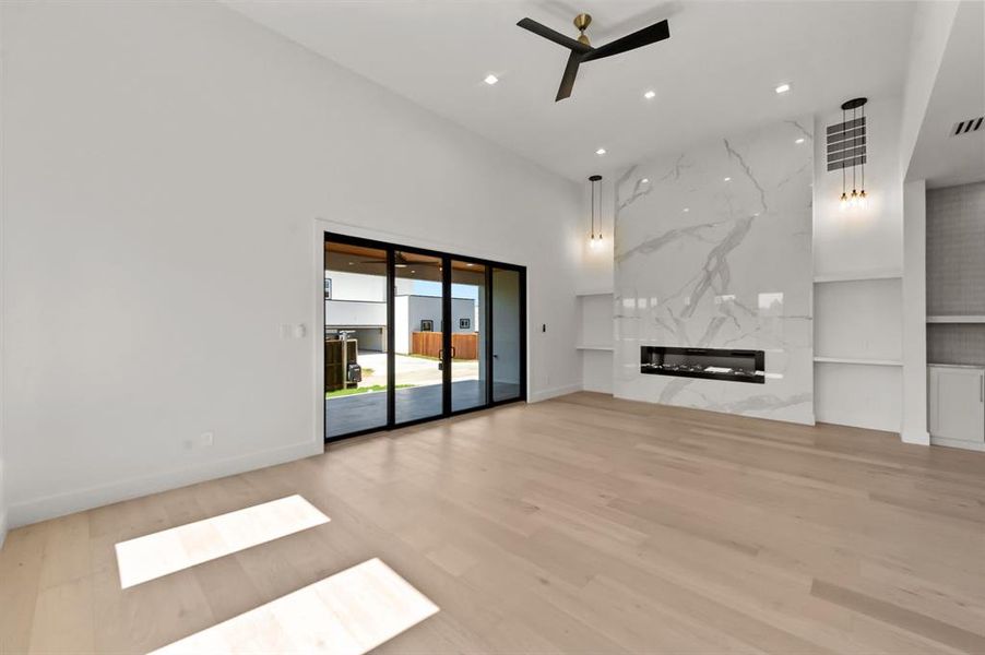 Living room with ceiling fan, a fireplace, a towering ceiling, and light hardwood / wood-style floors