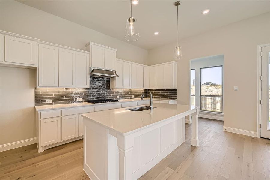 Kitchen with black gas cooktop, a center island with sink, decorative light fixtures, sink, and white cabinetry