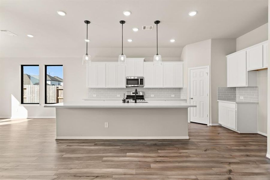 This light and bright kitchen features a large quartz island, white cabinets, a large sink overlooking your family room, recessed lighting, and beautiful backsplash.