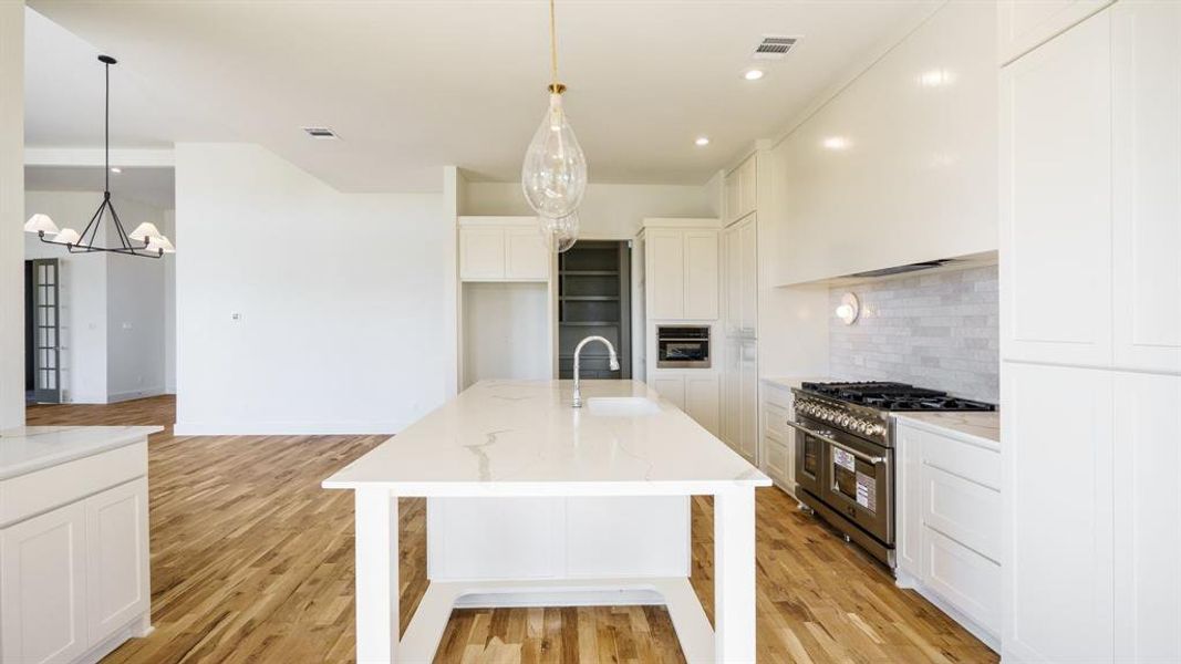 Kitchen featuring light hardwood / wood-style floors, sink, an island with sink, and double oven range