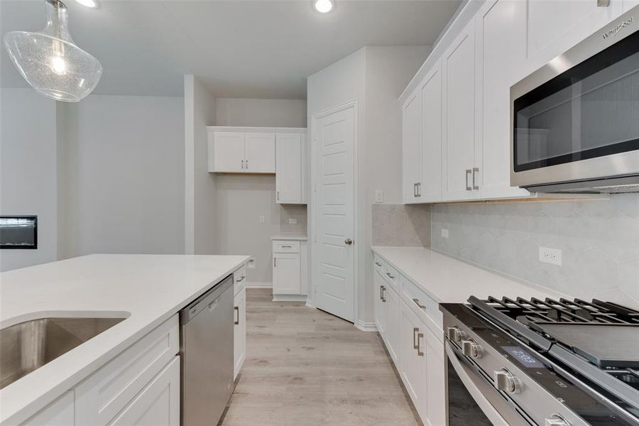 Kitchen featuring appliances with stainless steel finishes, decorative light fixtures, backsplash, light wood-type flooring, and white cabinetry