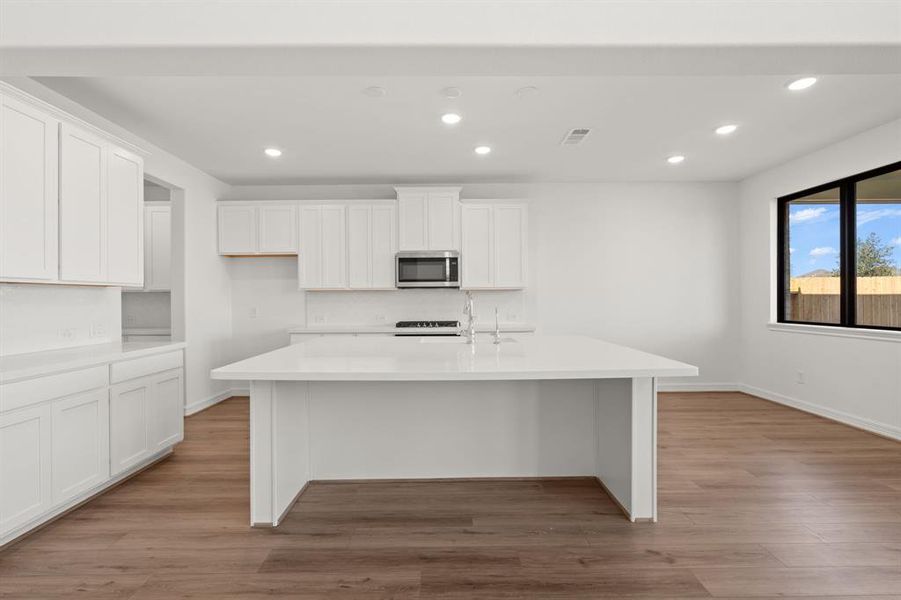 This light and bright kitchen features a large quartz island, white cabinets, a large sink overlooking your family room, recessed lighting, and beautiful backsplash.