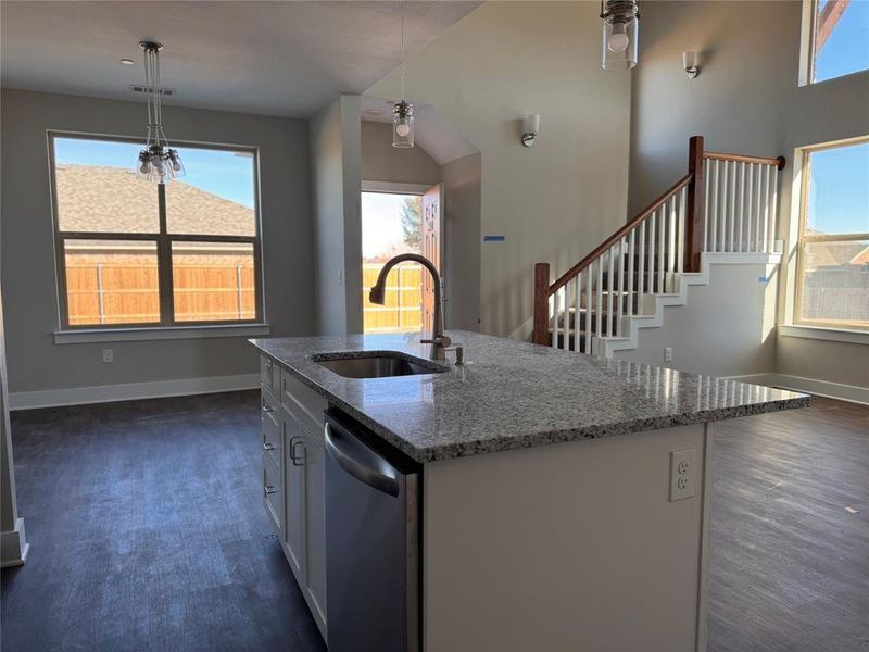 Kitchen featuring sink, an island with sink, stone counters, decorative light fixtures, and stainless steel dishwasher