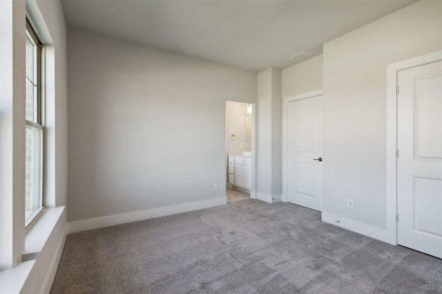 Unfurnished bedroom with ensuite bathroom and light colored carpet