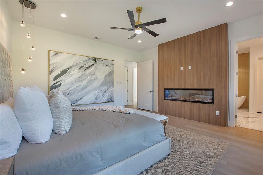 Bedroom with ceiling fan, light wood-type flooring, ensuite bathroom, and a large fireplace