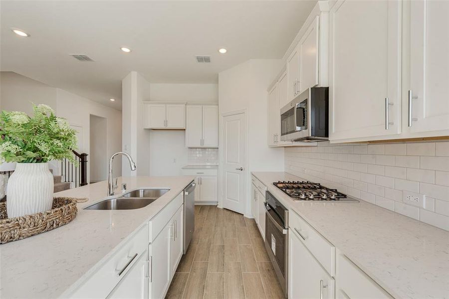 Kitchen featuring light stone counters, sink, white cabinetry, stainless steel appliances, and backsplash