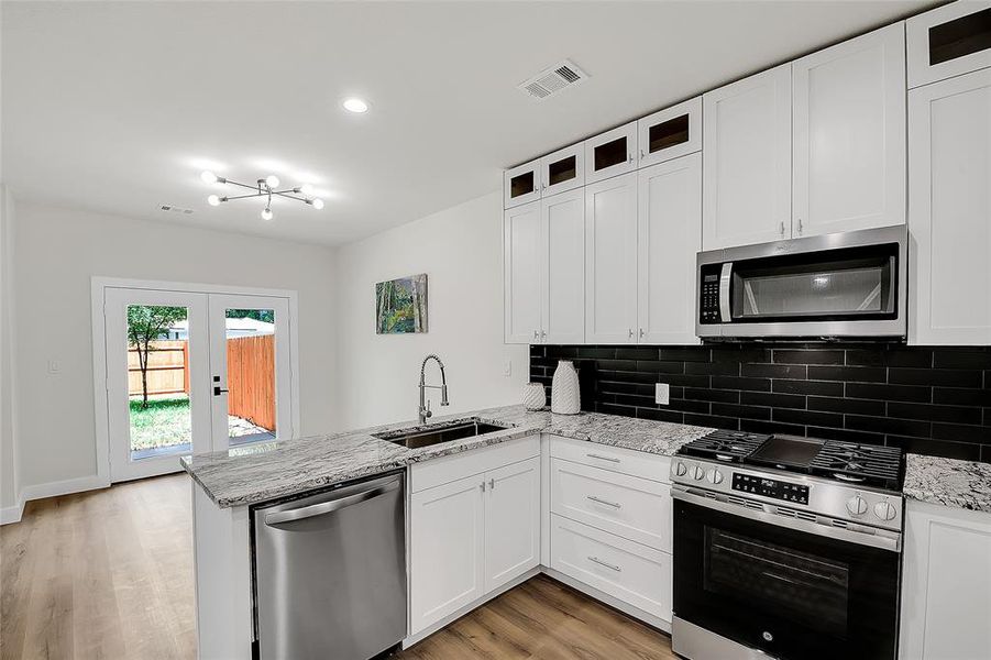 Kitchen and dining area granite peninsula, white cabinetry, stainless steel appliances, and light wood-type flooring