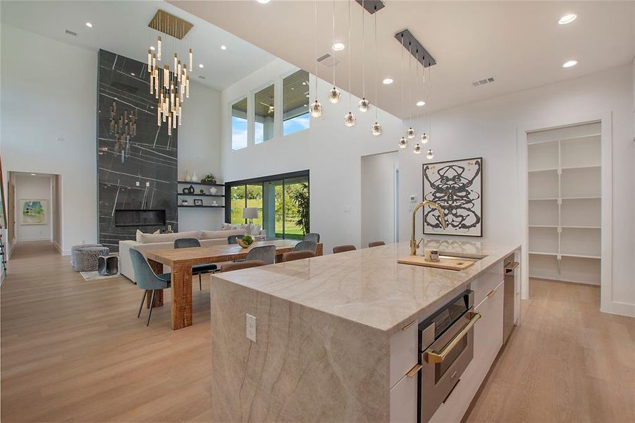 Kitchen with light stone counters, pendant lighting, sink, a kitchen island with sink, and oven