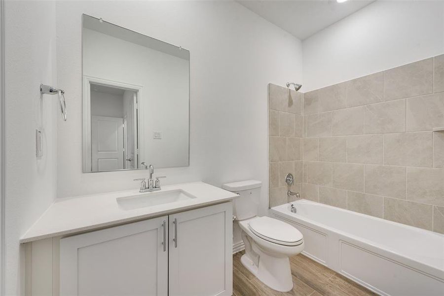 Full bathroom featuring tiled shower / bath, vanity, hardwood / wood-style flooring, and toilet