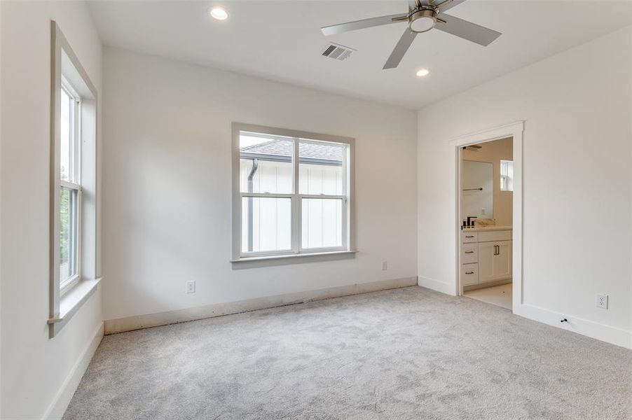 Unfurnished bedroom featuring light colored carpet, ensuite bathroom, and ceiling fan