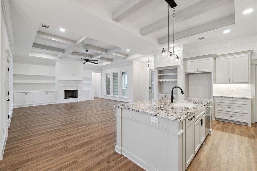 Kitchen with white cabinetry, light hardwood / wood-style flooring, a kitchen island with sink, coffered ceiling, and sink