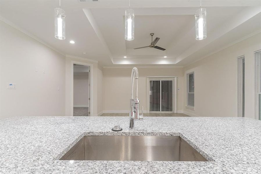Kitchen featuring decorative light fixtures, ceiling fan, sink, light stone counters, and DOUBLE raised ceiling