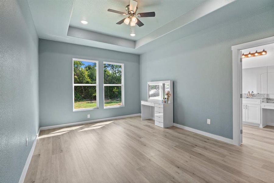 Unfurnished bedroom with ensuite bath, a raised ceiling, light hardwood / wood-style flooring, and ceiling fan