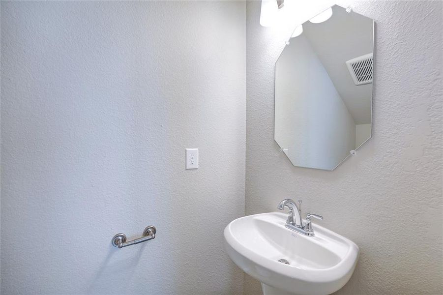 Enjoy a sleek, compact half-bathroom, featuring a stylish wall-mounted sink and an eye-catching octagonal mirror. The space boasts a clean, minimalist design with a soothing neutral color palette, creating an elegant and inviting atmosphere.