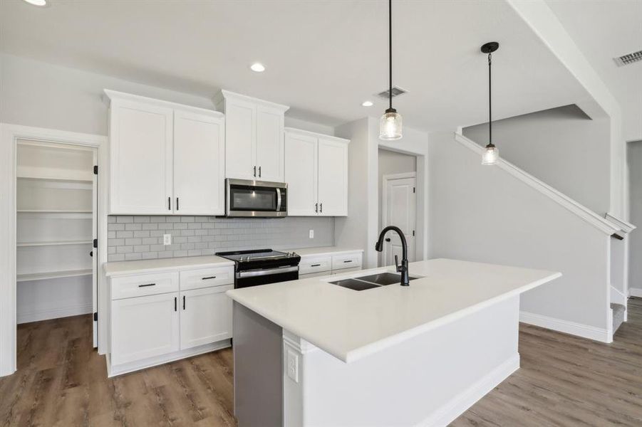 Kitchen with appliances with stainless steel finishes, white cabinets, sink, a kitchen island with sink, and hardwood / wood-style flooring