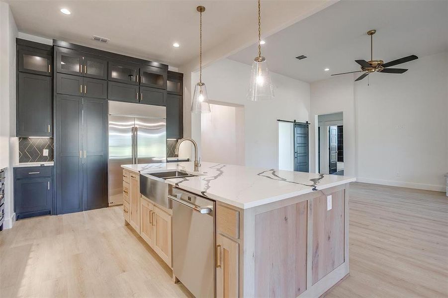 Kitchen featuring light hardwood / wood-style floors, light stone countertops, a center island with sink, appliances with stainless steel finishes, and backsplash