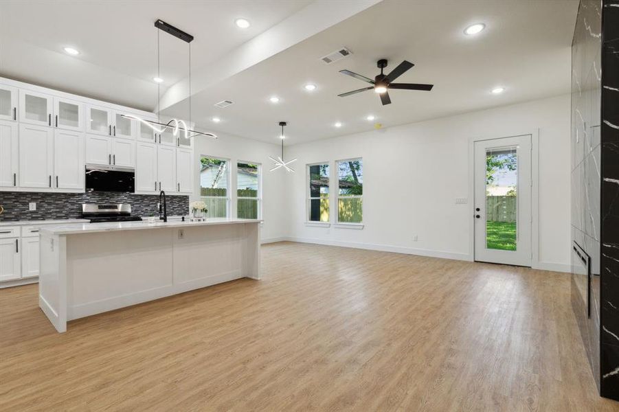 Kitchen featuring a center island with sink, stainless steel stove, hanging light fixtures, ceiling fan, and white cabinets