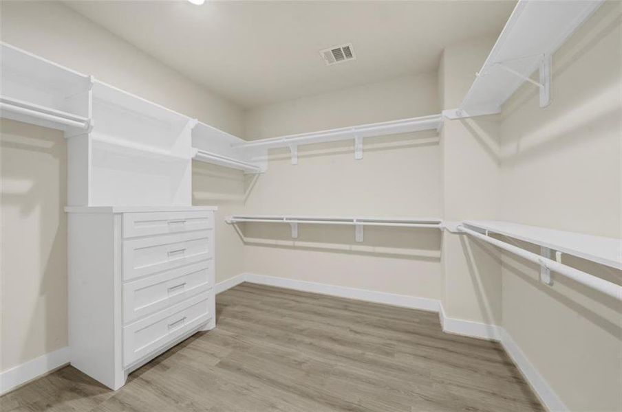 Super large and accommodating primary closet with organizational drawers and shelving.